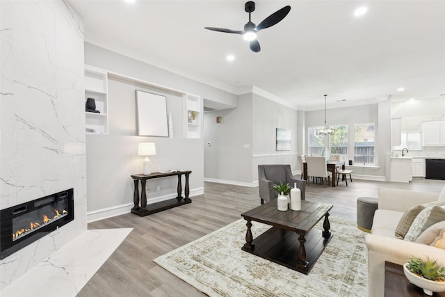 living area with a ceiling fan, ornamental molding, light wood finished floors, recessed lighting, and a high end fireplace