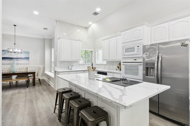kitchen with black appliances, white cabinetry, a breakfast bar area, a center island, and light stone countertops