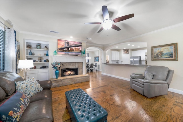 living area with arched walkways, a ceiling fan, wood finished floors, baseboards, and ornamental molding