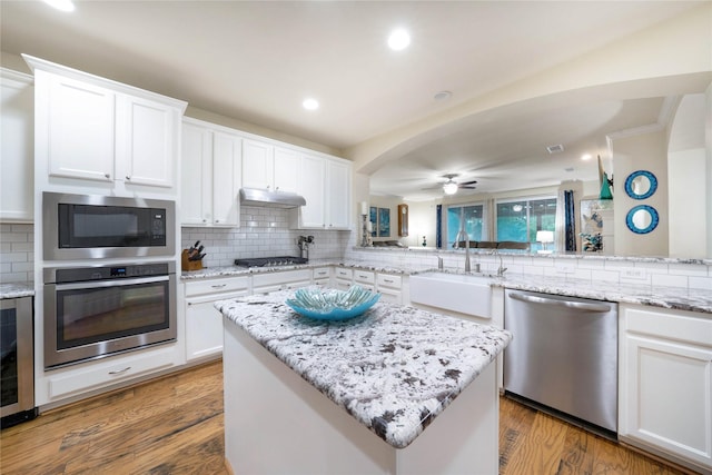 kitchen with appliances with stainless steel finishes, a sink, backsplash, arched walkways, and beverage cooler