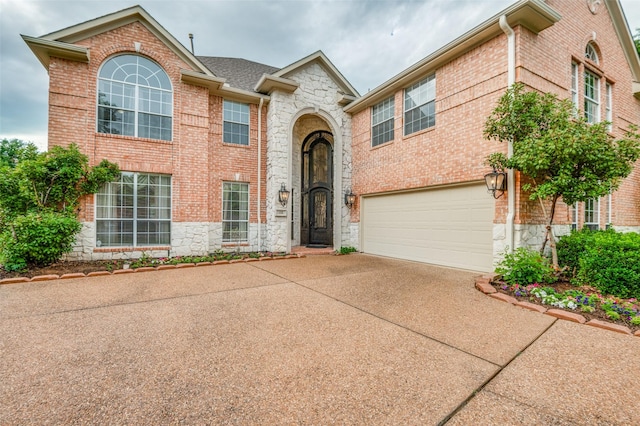 view of front facade featuring stone siding, driveway, an attached garage, and brick siding