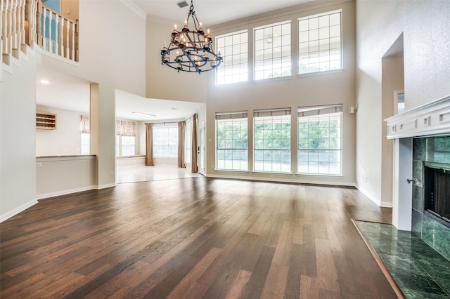 unfurnished living room featuring wood finished floors, a chandelier, a fireplace, a towering ceiling, and crown molding