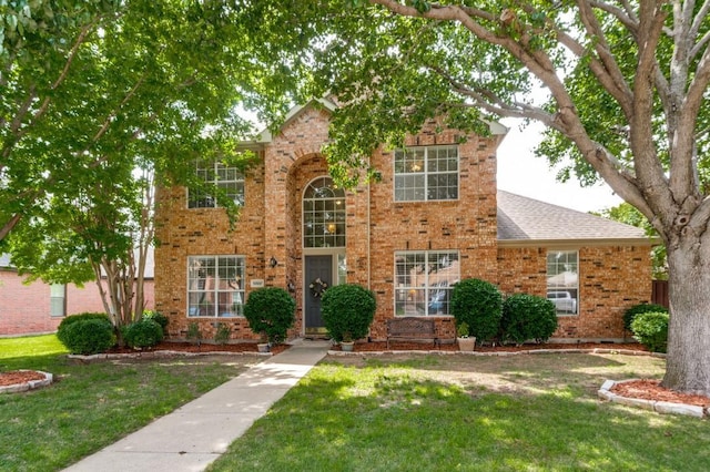 traditional home featuring a front yard, brick siding, and a shingled roof