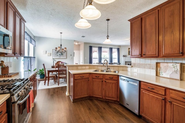 kitchen with stainless steel appliances, a sink, dark wood finished floors, a peninsula, and light countertops