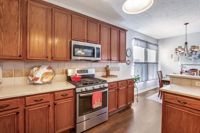 kitchen featuring appliances with stainless steel finishes, a chandelier, brown cabinets, backsplash, and a textured ceiling