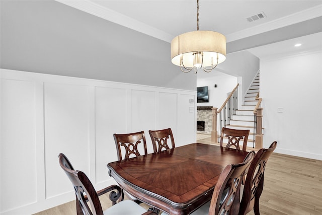 5250 Pueblo Ln, Frisco, TX 75034 - dining room with a decorative wall, light wood-type flooring, crown molding, a stone fireplace, and a chandelier