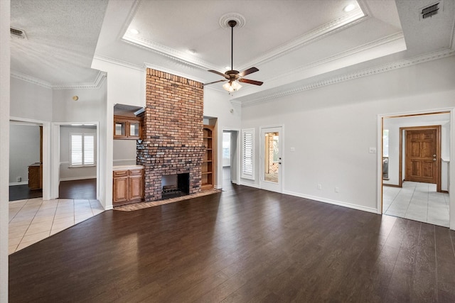 unfurnished living room featuring a towering ceiling, ceiling fan, crown molding, light wood finished floors, and a tray ceiling