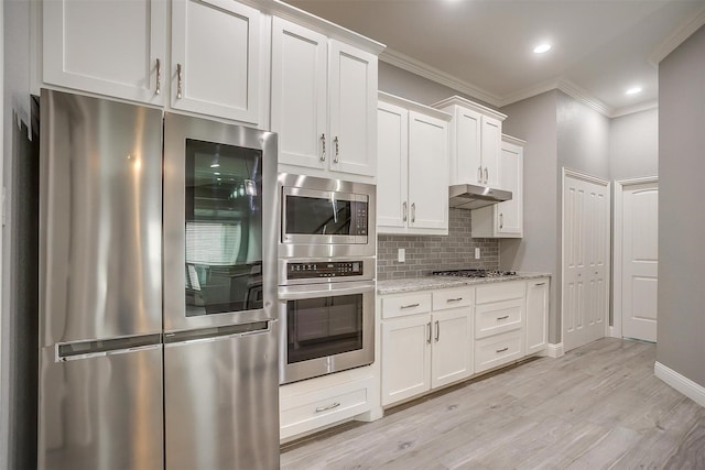 kitchen featuring appliances with stainless steel finishes, ornamental molding, decorative backsplash, under cabinet range hood, and light wood-style flooring