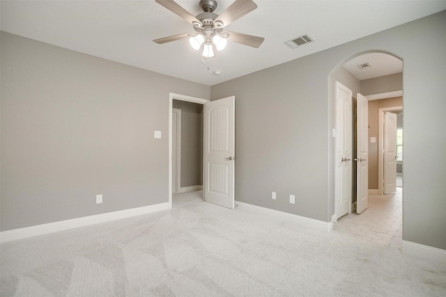 unfurnished bedroom featuring arched walkways, light colored carpet, a ceiling fan, and baseboards