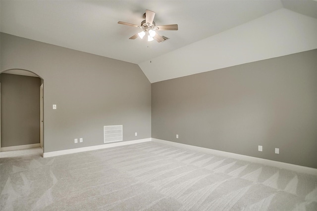 unfurnished room featuring arched walkways, ceiling fan, light carpet, vaulted ceiling, and baseboards