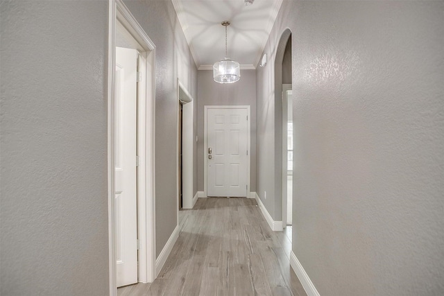 hallway with light wood-style floors, a textured wall, baseboards, arched walkways, and crown molding