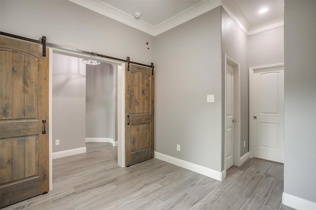 unfurnished bedroom featuring a barn door, light wood-type flooring, ornamental molding, and baseboards
