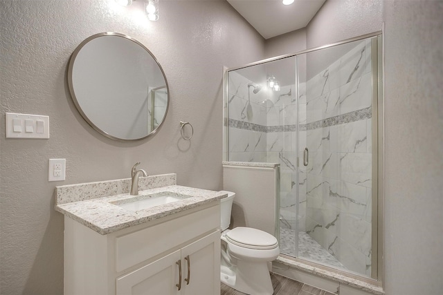 bathroom with a textured wall, a shower stall, toilet, vanity, and wood finished floors