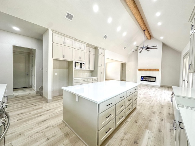 196 Jim Walter Dr, Runaway Bay, TX 76426 - kitchen with stainless steel microwave, beamed ceiling, light wood-style flooring, a glass covered fireplace, and light countertops