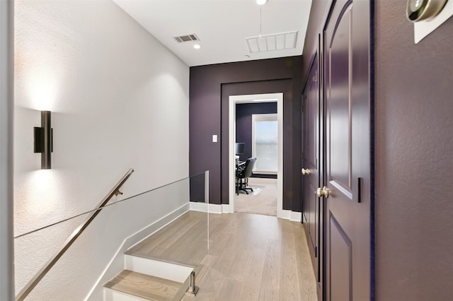 hall with light wood-style floors, baseboards, and attic access