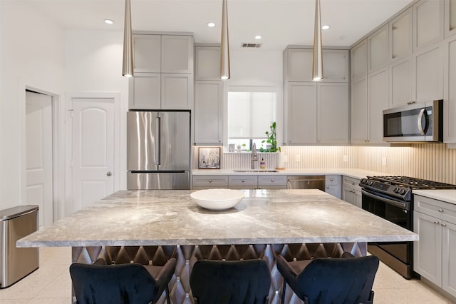 kitchen with stainless steel appliances, a sink, a kitchen breakfast bar, decorative backsplash, and a center island