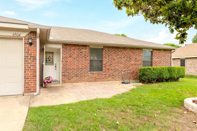 entrance to property with brick siding, a yard, a garage, and a shingled roof
