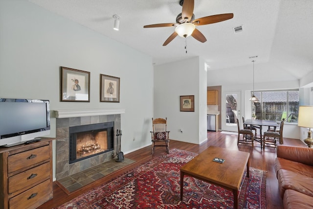 living area featuring a ceiling fan, a tile fireplace, dark wood-type flooring, and vaulted ceiling
