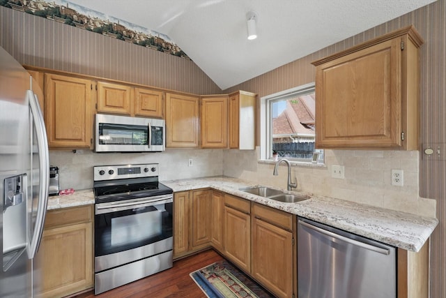 kitchen featuring stainless steel appliances, a sink, vaulted ceiling, dark wood-style floors, and light stone countertops