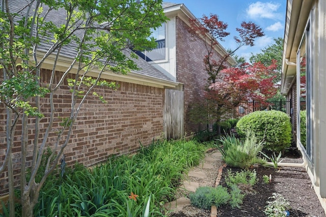 view of home's exterior with brick siding, fence, and a shingled roof