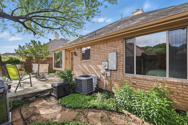 rear view of property featuring central AC, brick siding, a chimney, and a deck