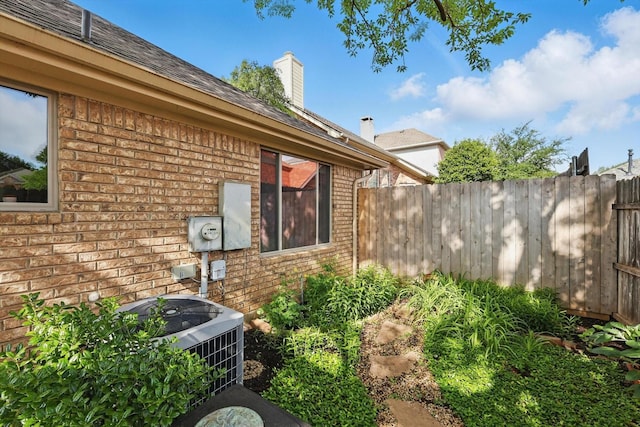 view of home's exterior with brick siding, fence, central AC unit, and a chimney