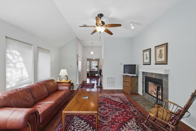 living room featuring ceiling fan, wood finished floors, baseboards, vaulted ceiling, and a tiled fireplace