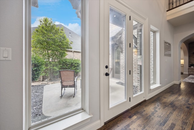 entryway with arched walkways, dark wood-style flooring, and baseboards