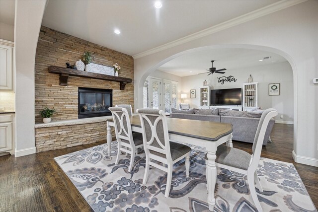 dining room featuring a stone fireplace, wood finished floors, arched walkways, baseboards, and ornamental molding