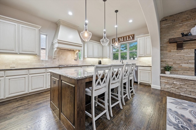 580 Butchart Dr, Prosper, TX 75078 - kitchen featuring custom range hood, decorative backsplash, a kitchen island, a breakfast bar area, and dark wood finished floors