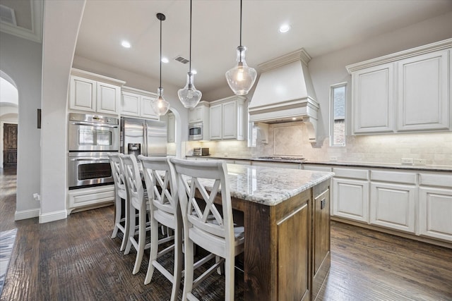 580 Butchart Dr, Prosper, TX 75078 - kitchen with arched walkways, stainless steel appliances, a kitchen island, custom range hood, and decorative backsplash