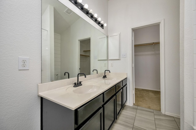 6717 Red Rock Trl, Watauga, TX 76137 - bathroom featuring a walk in closet, double vanity, tile patterned flooring, and a textured wall