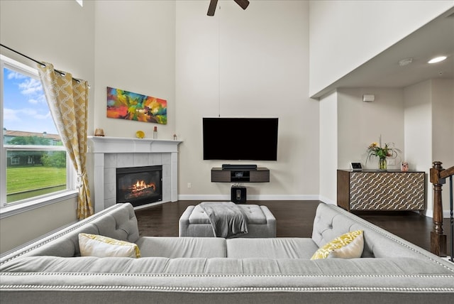 living area featuring a towering ceiling, wood finished floors, baseboards, a tile fireplace, and ceiling fan