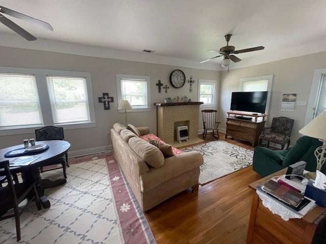 living area with a ceiling fan, wood finished floors, baseboards, and a brick fireplace