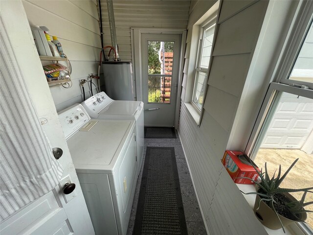 laundry area with water heater, separate washer and dryer, and wood walls