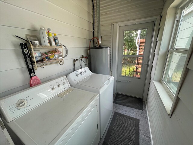 clothes washing area with gas water heater, independent washer and dryer, and wooden walls
