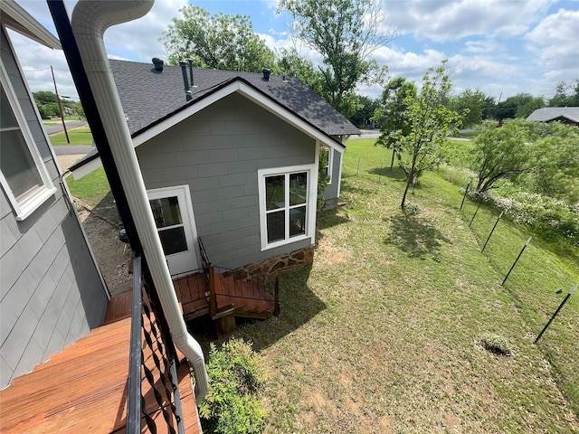 view of side of property with a shingled roof, a yard, and a deck