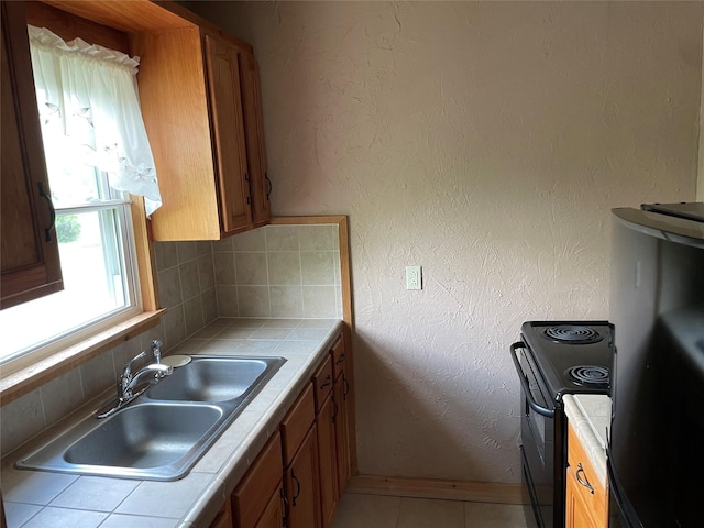 kitchen featuring tile counters, a sink, black range with electric cooktop, backsplash, and brown cabinets