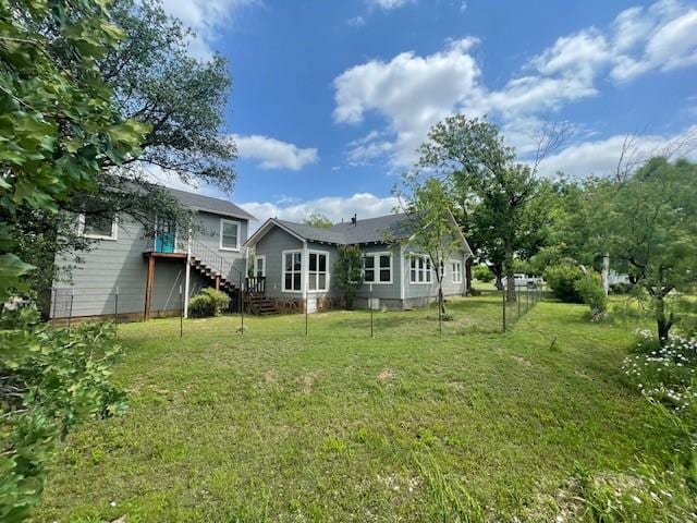 rear view of property with stairway and a lawn