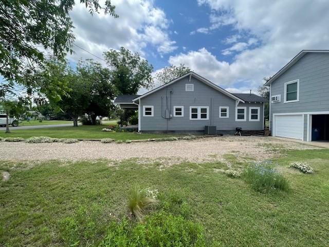 back of house with a garage, cooling unit, and a lawn