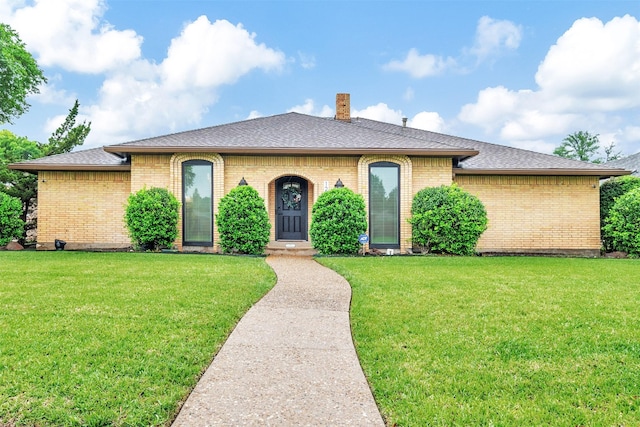 view of front facade featuring brick siding, a front yard, a chimney, and a shingled roof