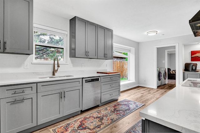 kitchen with stainless steel dishwasher, washing machine and clothes dryer, a sink, and gray cabinetry