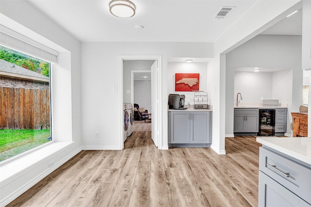 bar area with wine cooler, washer and dryer, light wood-style flooring, baseboards, and a sink