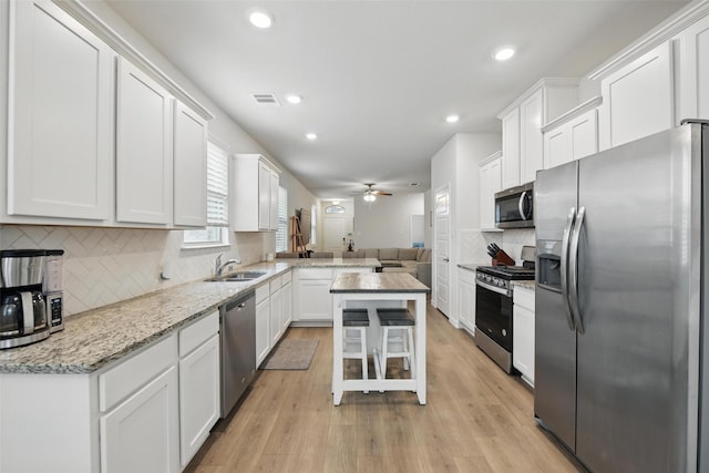 kitchen featuring appliances with stainless steel finishes, a sink, a ceiling fan, white cabinetry, and decorative backsplash
