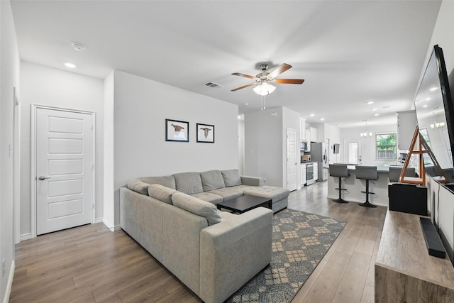 living area with a chandelier, a ceiling fan, wood finished floors, recessed lighting, and baseboards