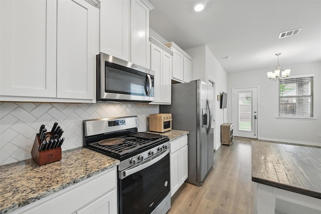 kitchen featuring appliances with stainless steel finishes, white cabinets, decorative backsplash, a chandelier, and light wood-type flooring