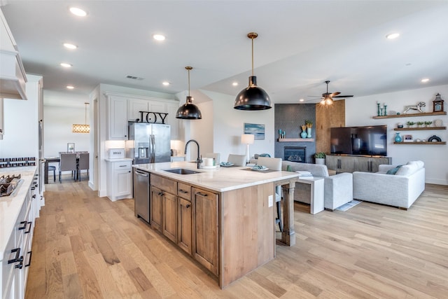 kitchen with a ceiling fan, a sink, stainless steel appliances, light wood finished floors, and white cabinets