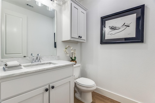 half bathroom featuring vanity, toilet, wood finished floors, and baseboards