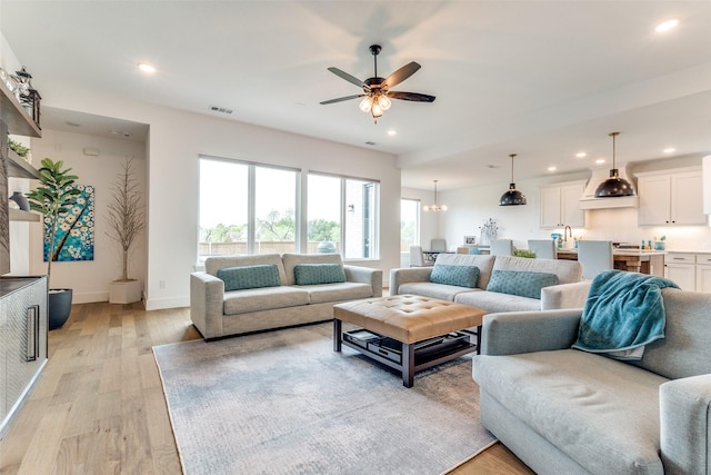 living room featuring light wood finished floors, ceiling fan, recessed lighting, baseboards, and a chandelier