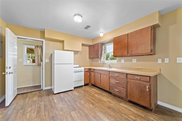 kitchen with white appliances, a sink, wood finished floors, brown cabinets, and baseboards